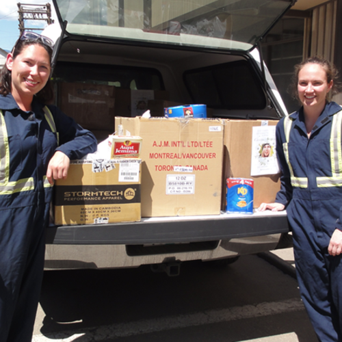 Two people in overalls stand by a truck loaded with boxes and canned goods.